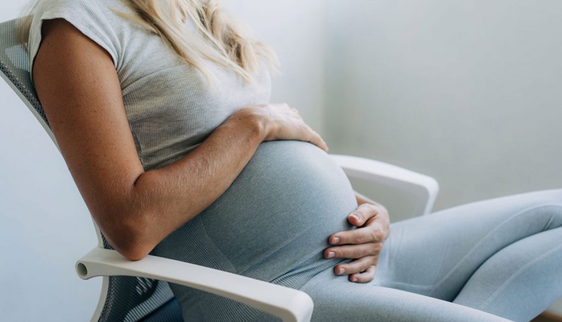 Woman holding her pregnant belly sitting in a chair
